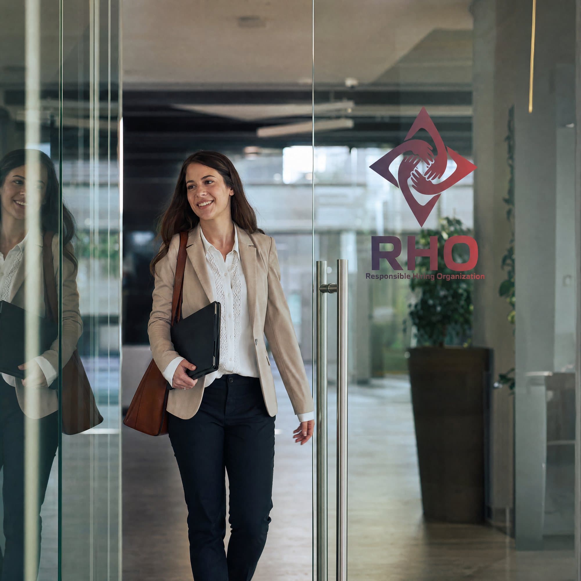 Woman with a shoulder bag and a folder walking through an office's glass doors