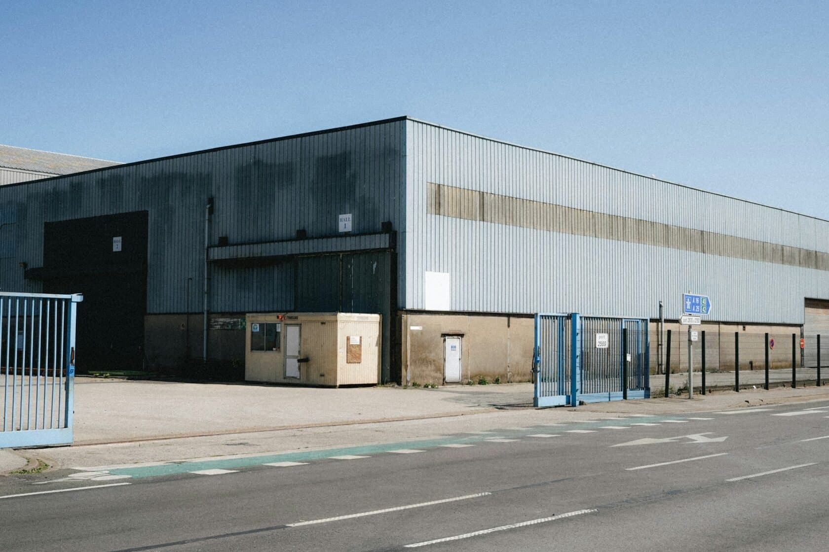 Long metal-clad industrial building with a gated yard beside the road